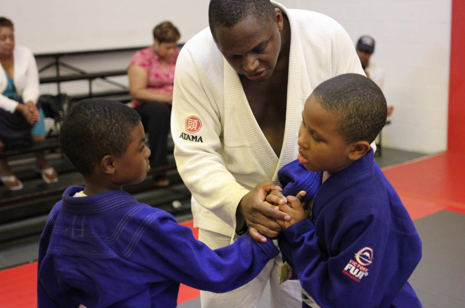 Judo coach guiding two young students through a grip at Baltimore Martial Arts Academy
