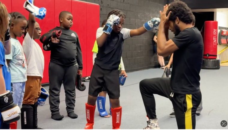 Coach Deon Jackson teaching a child to punch in kids Muay Thai, students wearing gloves and shin guards