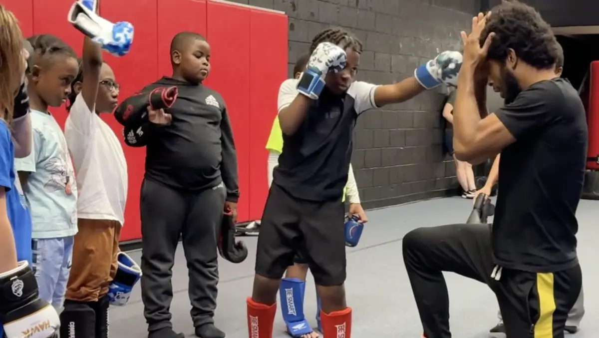 Coach Deon Jackson teaching guard position to a kids Muay Thai class